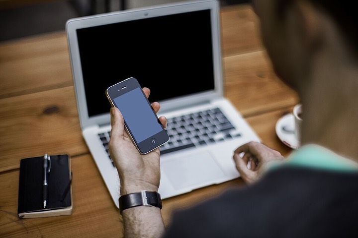Man holding a smartphone in front of an open laptop