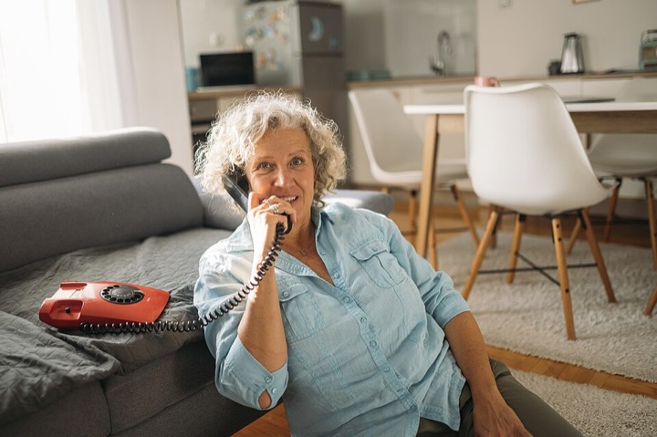 Older woman smiling as she talks on a corded landline phone at home