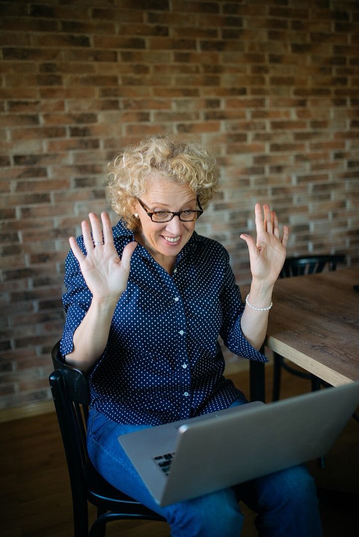 Older woman raising both hands and smiling during a video call on her laptop